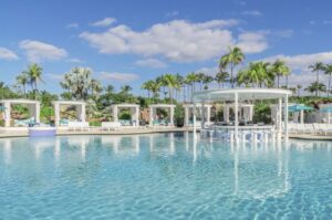 A pool with white chairs and palm trees in the background.